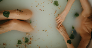Arms and legs rest above water in a bath filled with flowers, leaves, and herbs.