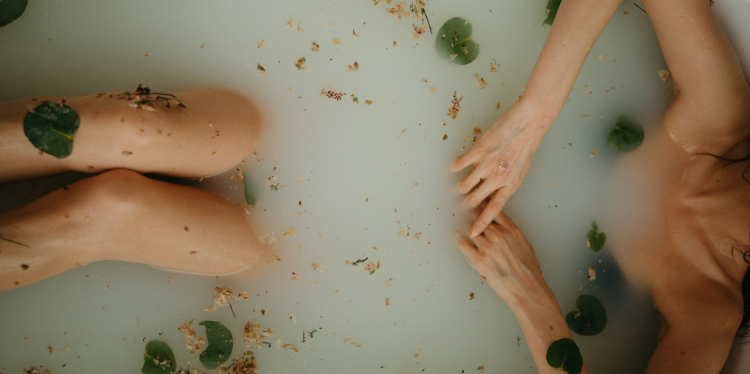 Arms and legs float above water in a luxurious bath with leaves, flowers, and herbs.