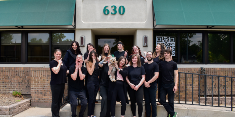 The team at Be Well Bodyworks stands out front of the business smiling and making silly faces in celebration of their 11 year anniversary.