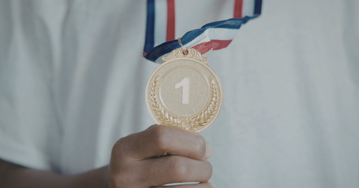 A person holds their winning 1st place, gold medal in front of themselves.